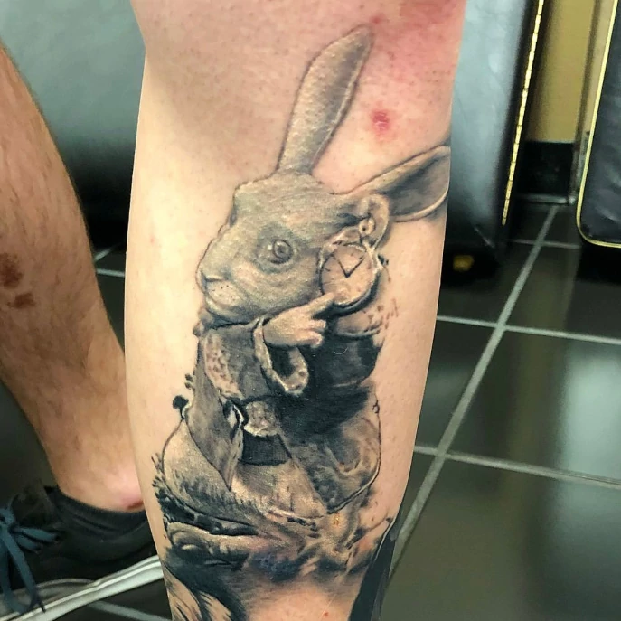 Sacred Mandala Studio tattoo artist - Russ Howie - calf tattoo in fine line black and grey of the late rabbit from Alice in Wonderland.